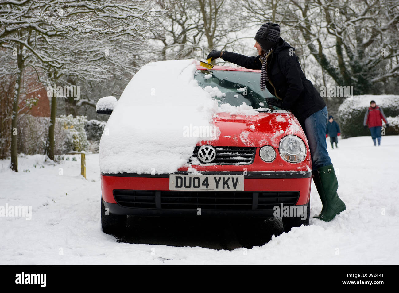 Una donna cancella neve pesante dalla sua auto prima di tentare di guidare a lavorare. La nevicata porta il caos per pendolari Foto Stock