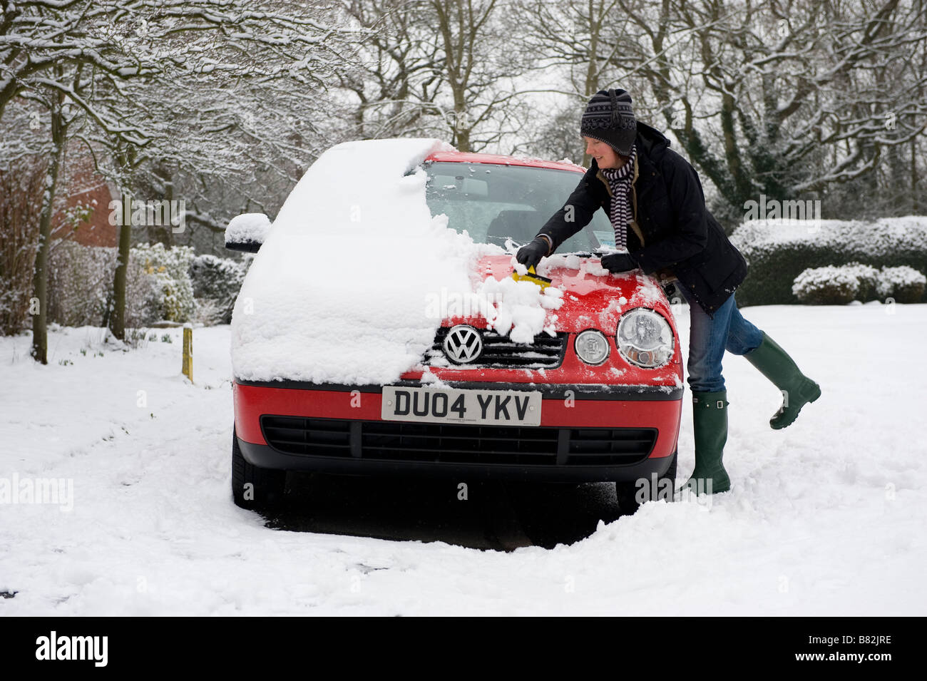 Una donna cancella neve pesante dalla sua auto prima di tentare di guidare a lavorare. La nevicata porta il caos per pendolari Foto Stock