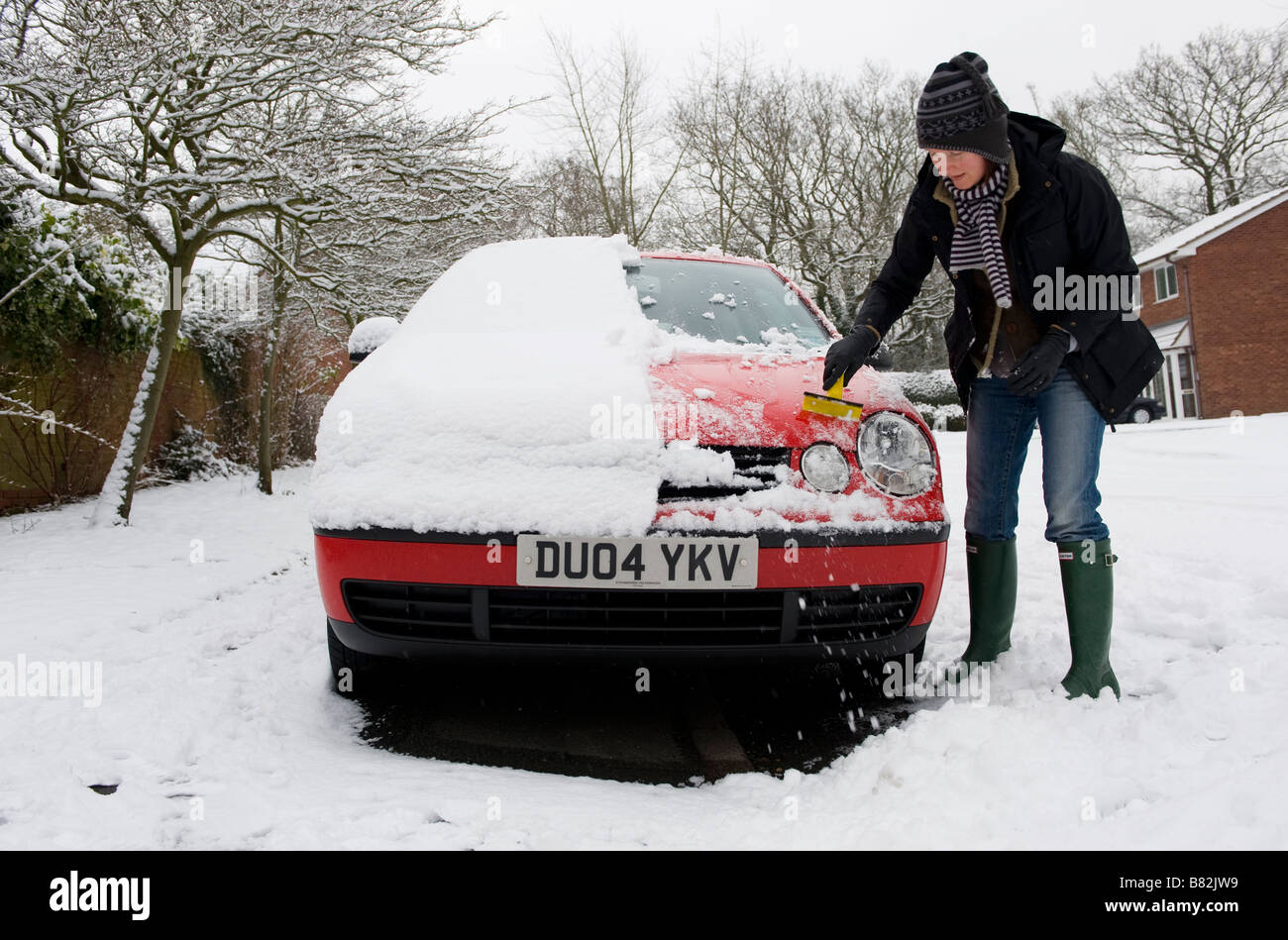 Una donna cancella neve pesante dalla sua auto prima di tentare di guidare a lavorare. La nevicata porta il caos per i pendolari Foto Stock