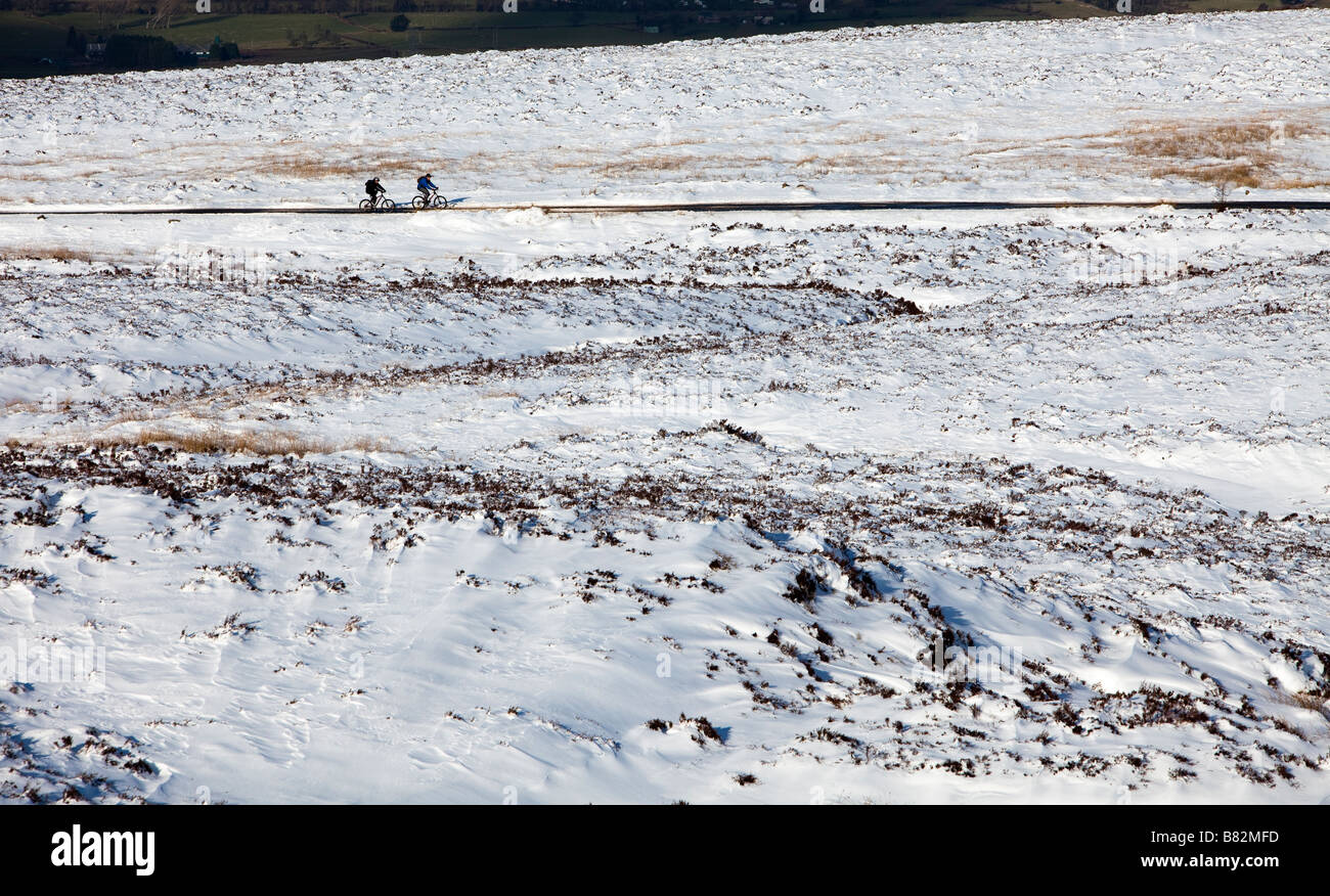 Due persone in bicicletta sul telecomando strada di montagna attraverso mori ricoperta di neve Pwll Du Wales UK Foto Stock
