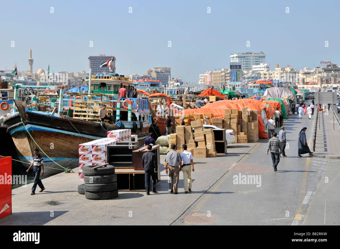 Lavoratori del Dubai Creek in barca sambuco e persone che camminano oltre Trasporto merci e merci su affollata banchina del porto congestionato United Arab Emirati Arabi Uniti Medio Oriente Foto Stock