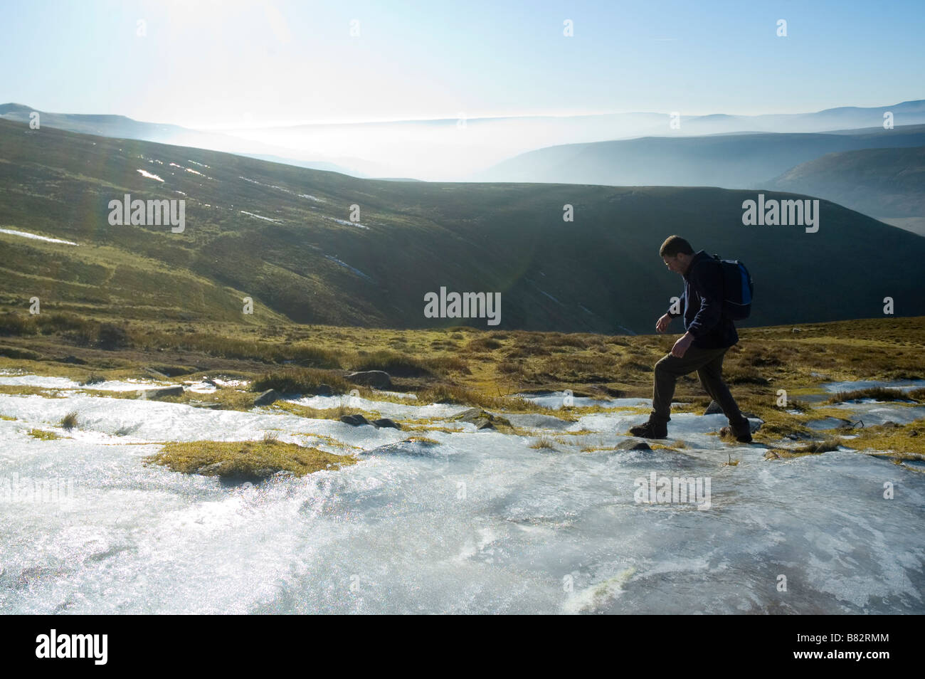 Un escursionista cammina davanti a una grande patch di ghiaccio in montagna nera Parco Nazionale di Brecon Beacons Powys Galles Centrale Regno Unito Foto Stock