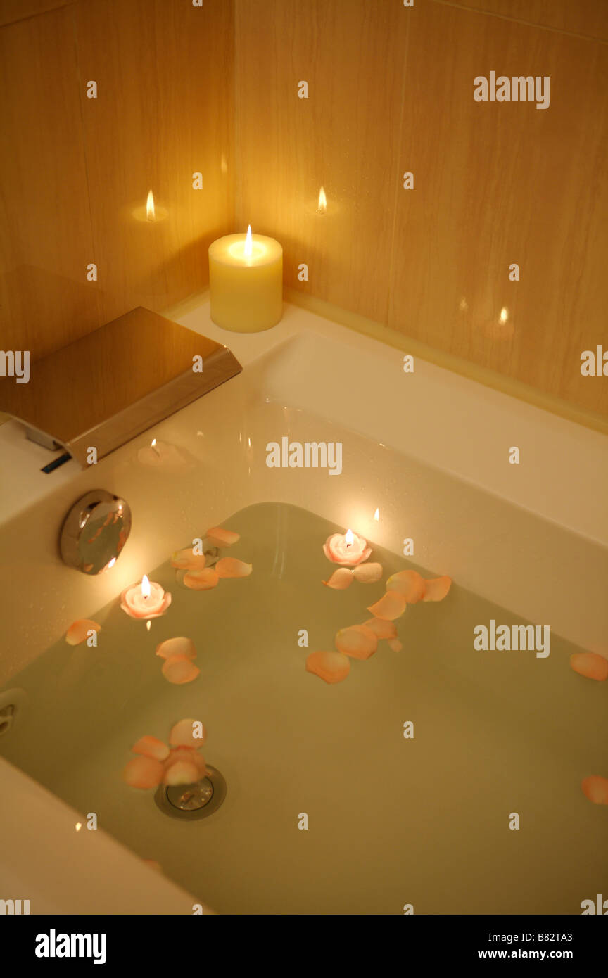 Vasca da bagno piena di acqua e petali con candela che brucia sul bordo Foto Stock