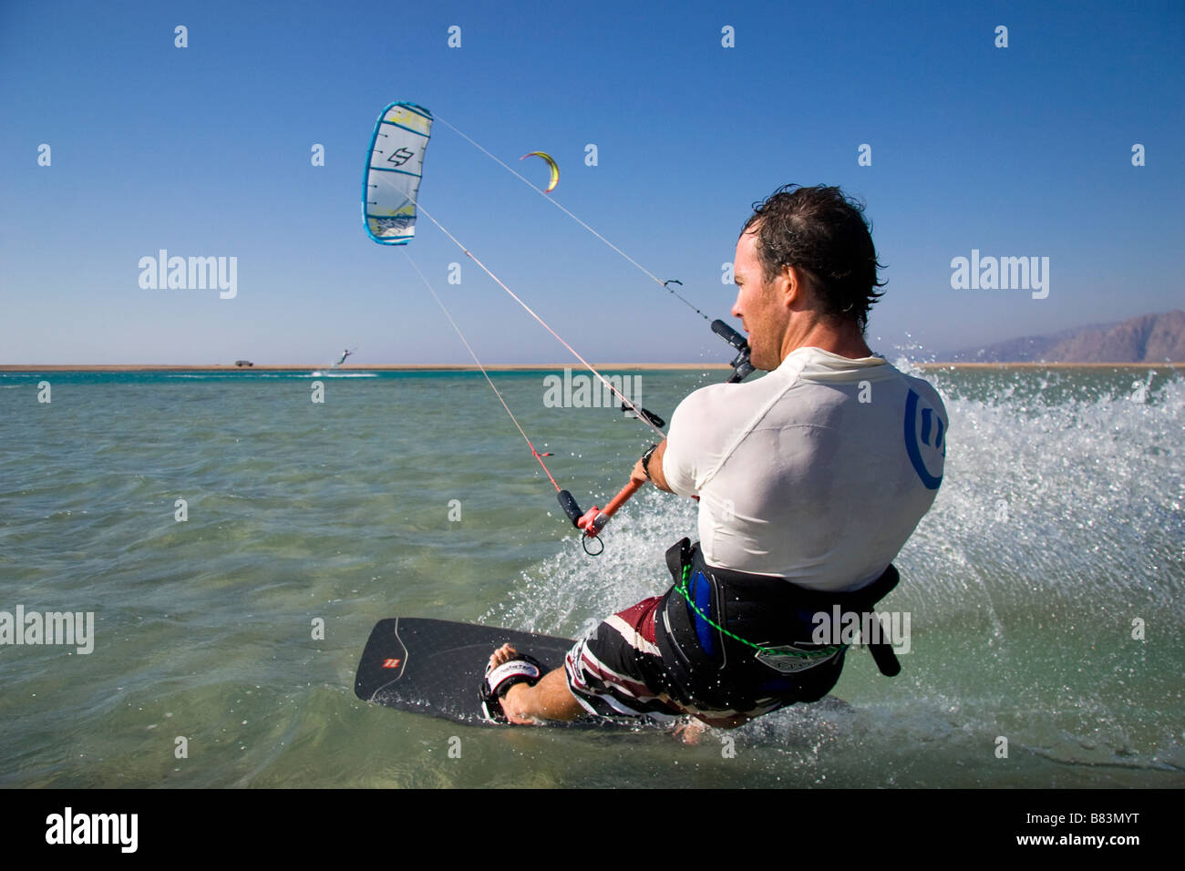 Un kitesurfer attraversa il turchese acqua piatta laguna (QURA BAY) all'interno della sabbia sputa nel Sinai resort di Dahab in Egitto Foto Stock