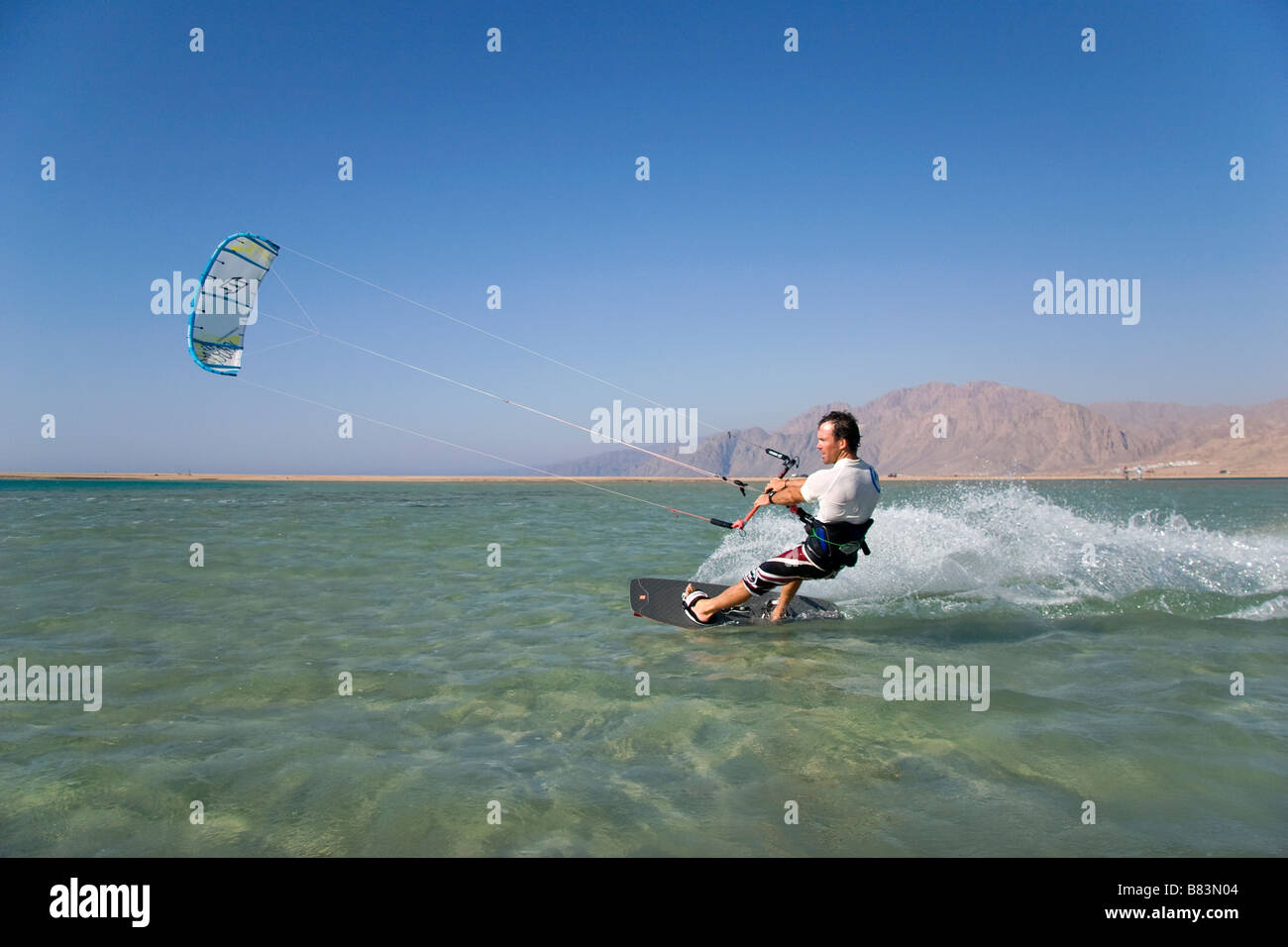 Un kitesurfer attraversa il turchese acqua piatta laguna (QURA BAY) all'interno della sabbia sputa nel Sinai resort di Dahab in Egitto Foto Stock