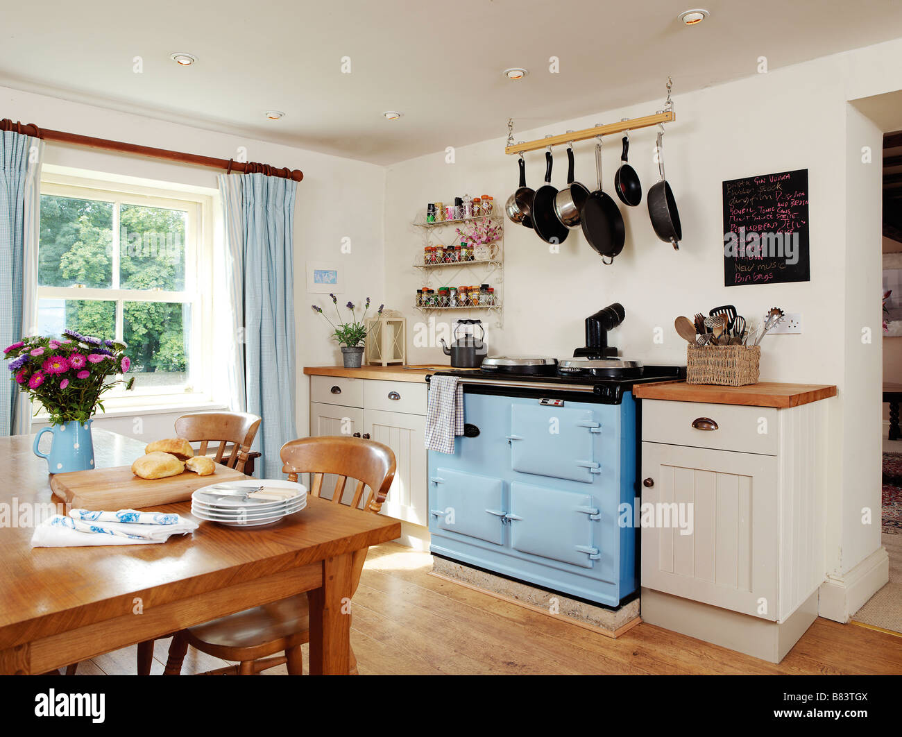 In stile country cucina con blue aga e tavolo per la colazione con blackboard e padelle appeso sopra Foto Stock In stile country cucina con blue aga e tavolo per la colazione con blackboard e padelle appeso sopra Foto Stock