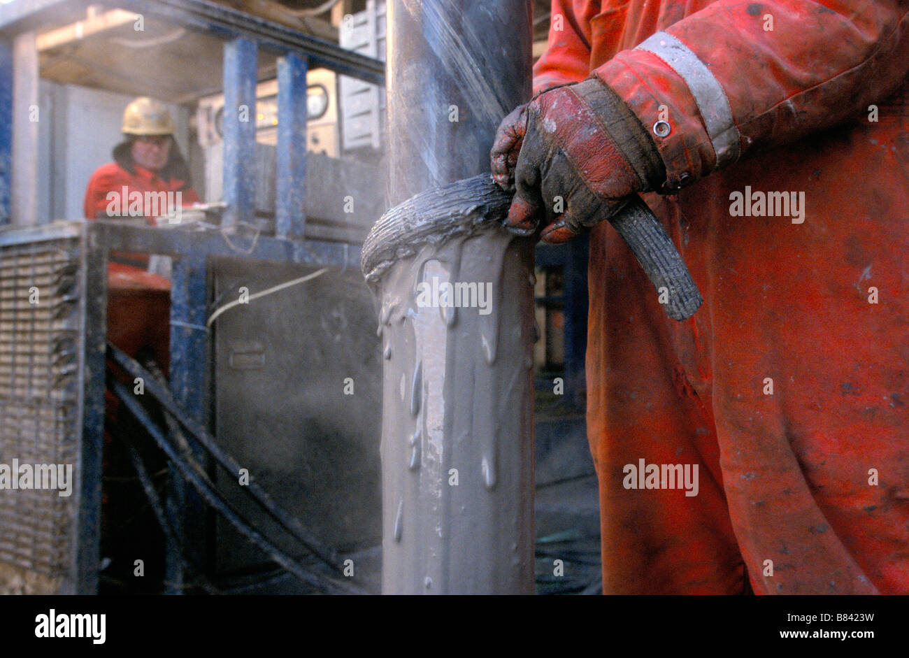 Lavoratori di olio su di una piattaforma di perforazione in Kazakhstan portare il tubo di raccordo coperti di fango di lubrificazione Foto Stock