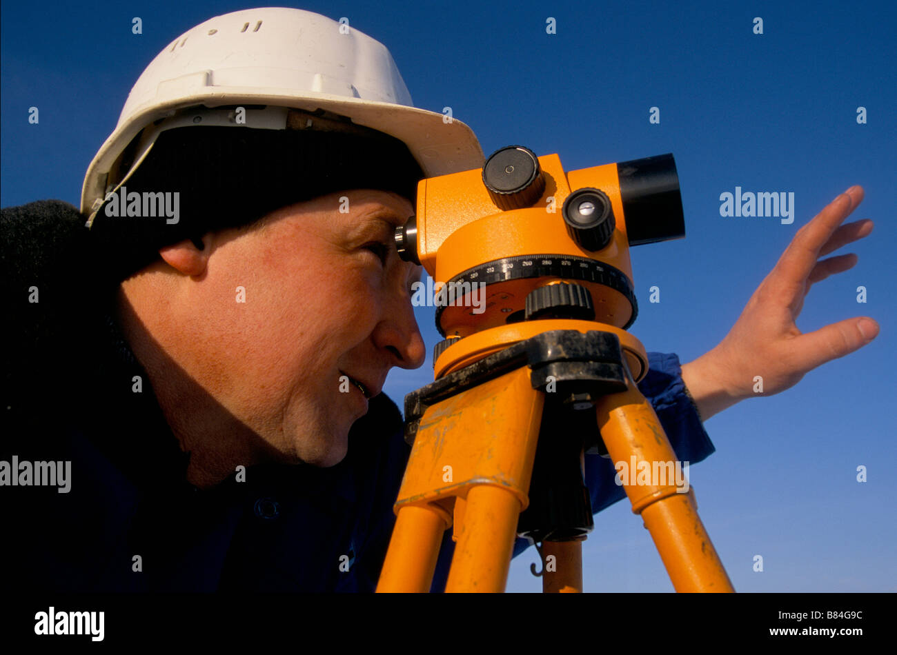 Un geometra segnali al suo collega con il personale di livellamento come egli utilizza il teodolite presso un impianto di olio in costruzione, Kazakistan Foto Stock