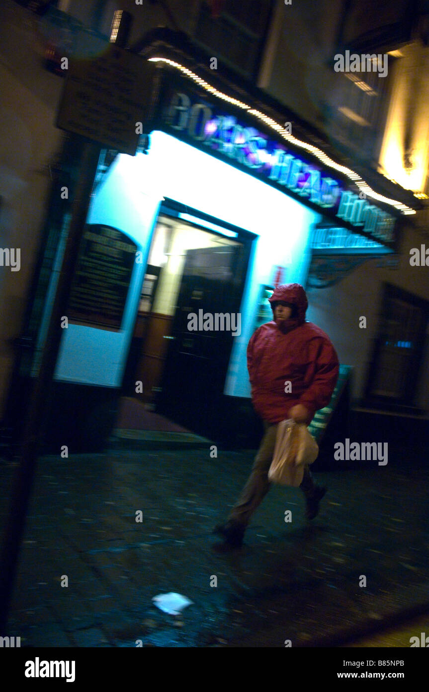 Un uomo cammina davanti a un pub su un umido e ventoso notte a Carmarthen Carmarthenshire Galles Regno Unito Europa Foto Stock