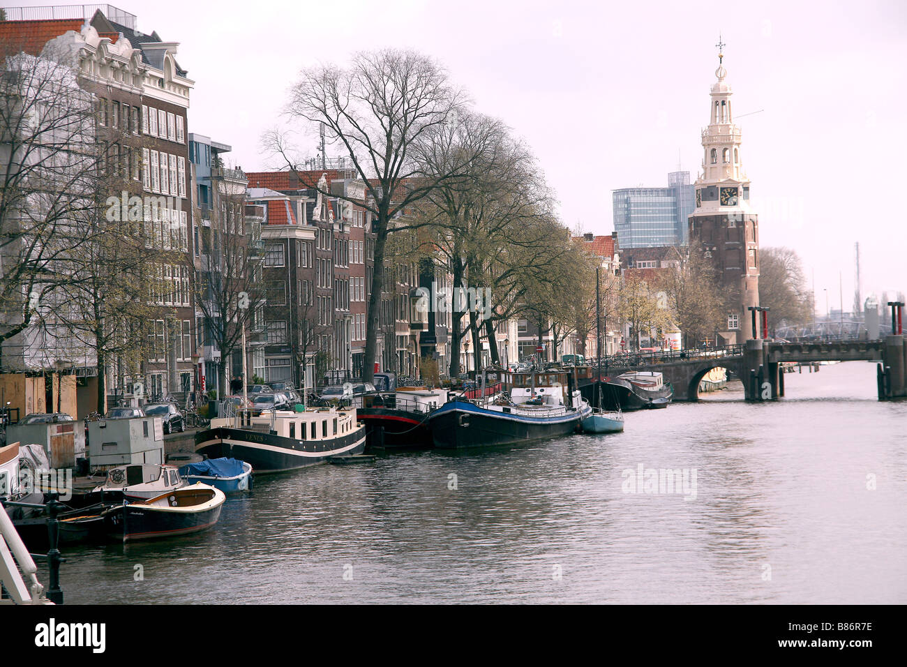 Barche e chiatte sul canale di Amsterdam con il ponte e la torre nel ponte di sfondo in Olanda Foto Stock