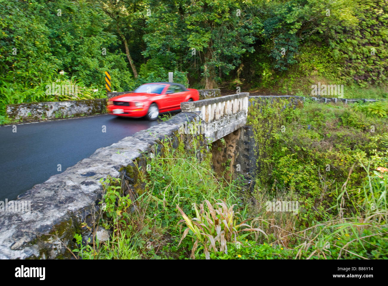 Il passaggio di un auto su uno dei tanti one-way di ponti sul Hana autostrada, a nord di Maui, Hawaii Foto Stock