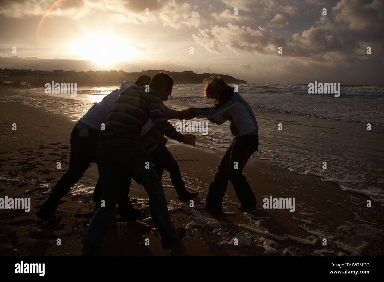 Silhouette gruppo di adolescenti amici studenti messing about su una spiaggia al tramonto Foto Stock