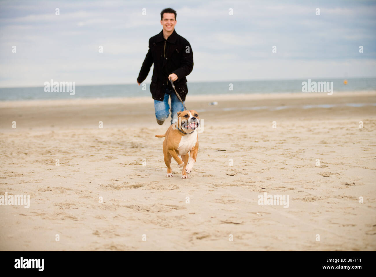 Giovane uomo che corre sulla spiaggia con un cane Foto Stock