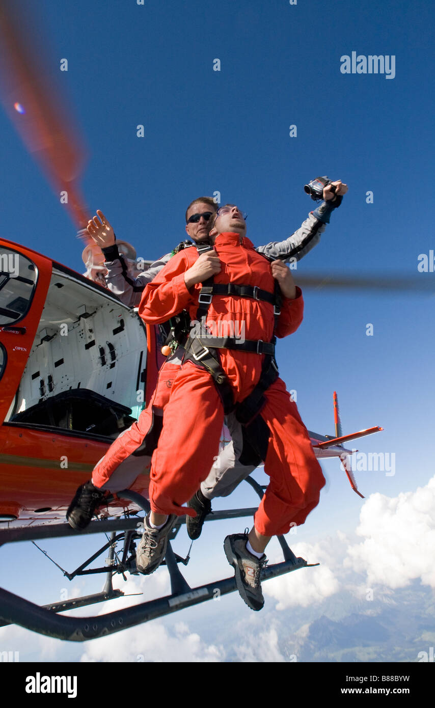 Tandem Skydive in uscita da un elicottero nel cielo blu e iniziare a tuffarsi in caduta libera collegati insieme come un giovane subacqueo Foto Stock