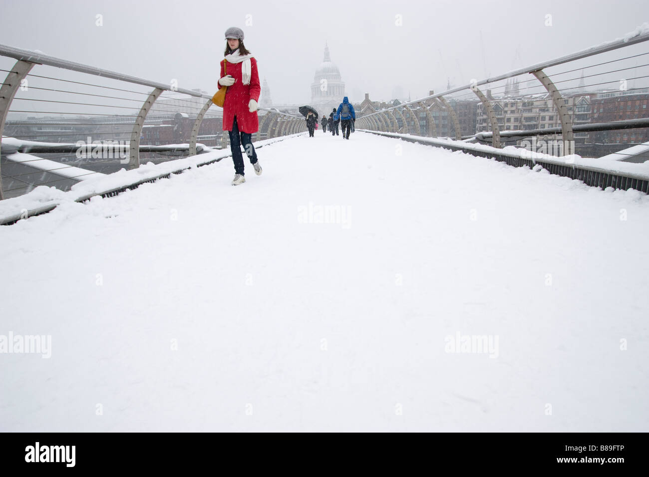 Donna in Red coat cammina nella fitta neve attraverso il Millennium Bridge con la St Pauls Cathedral in background, Londra Regno Unito, Foto Stock