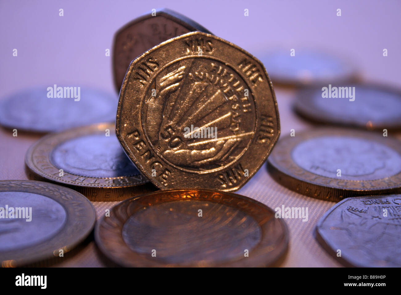 Una fotografia del NHS cinquanta pence pezzo circondato da due libbre di monete e altri UK GBP denaro Foto Stock