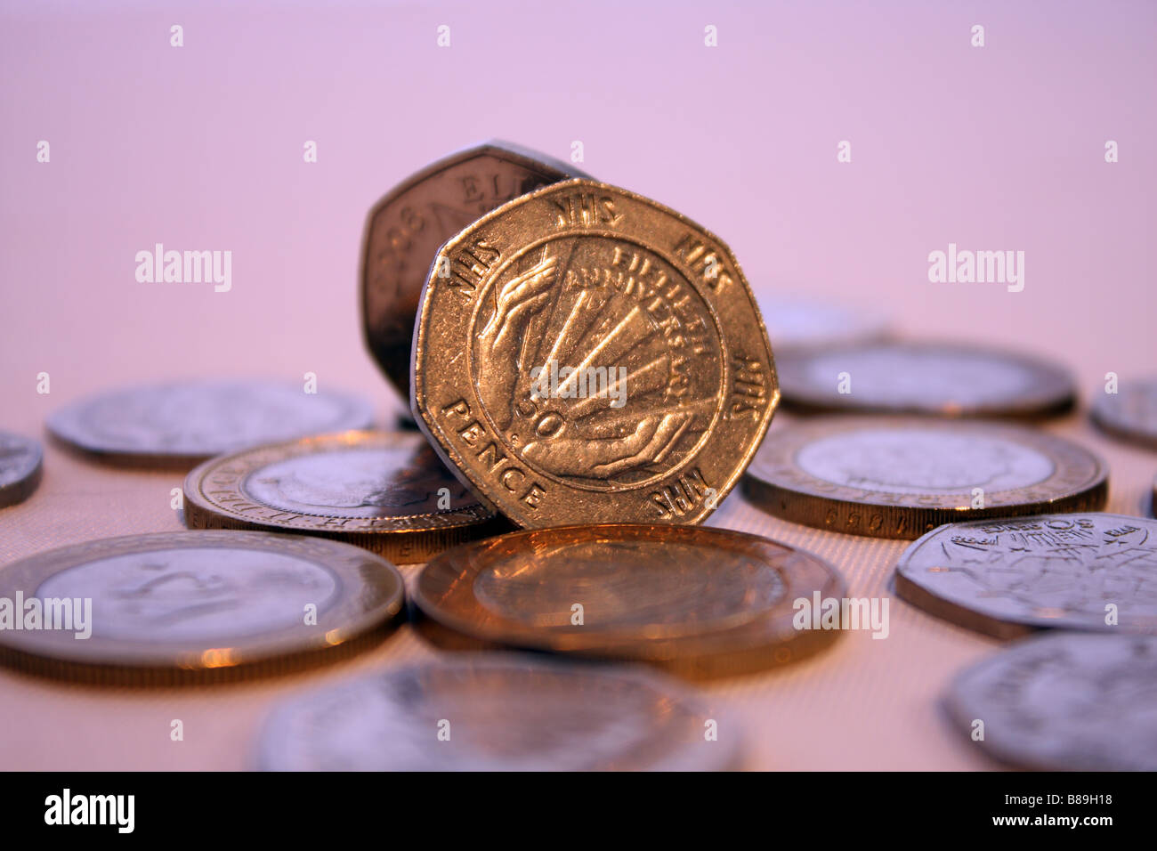 Una fotografia del NHS cinquanta pence pezzo circondato da due libbre di monete e altri UK GBP denaro Foto Stock