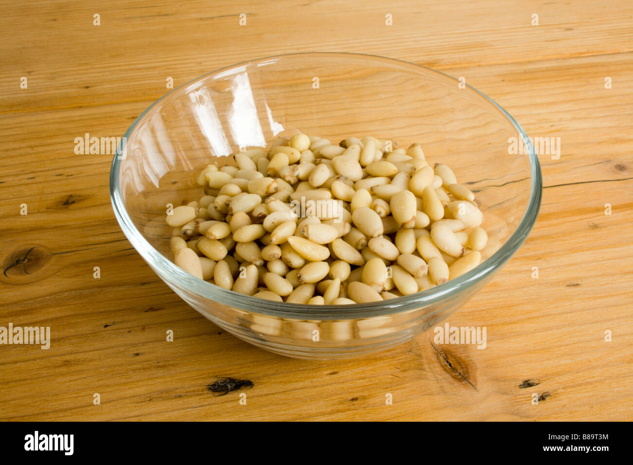 I pinoli in una ciotola di vetro su una tavola di pino. Foto Stock