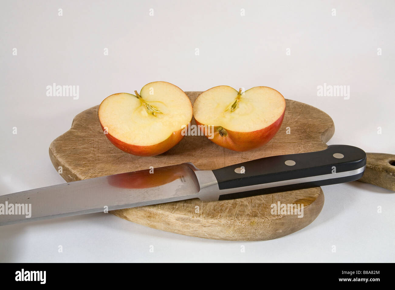 Due metà di una succosa mela su un tagliere affettato uniformemente con una grande cucina o coltello da prosciutto Foto Stock