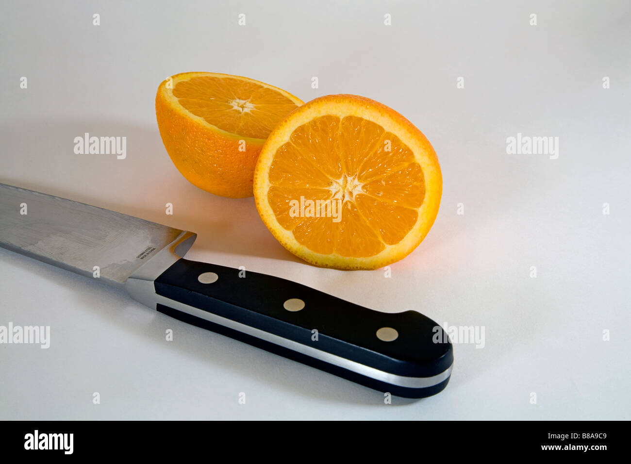 Ancora vita FRUTTA ORTAGGI due metà di una arancia navel affettato uniformemente in due da una grande cucina o coltello da prosciutto Foto Stock