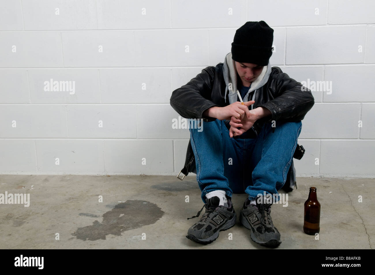 Ragazzo adolescente si siede con la schiena contro la parete, bere e fumare Foto Stock