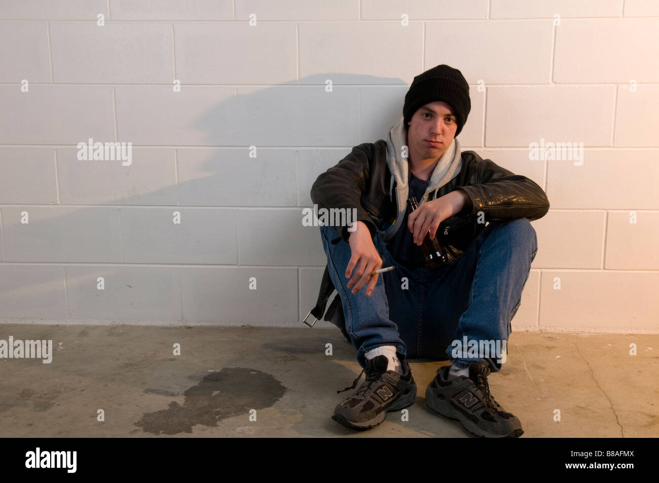 Ragazzo adolescente si siede con la schiena contro la parete, bere e fumare Foto Stock