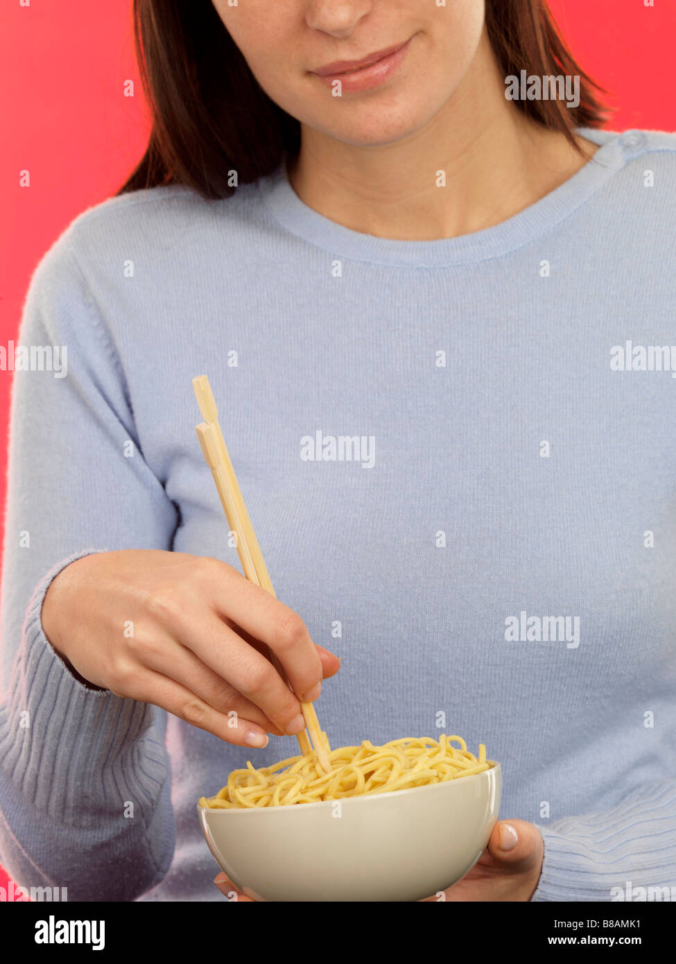 Giovane donna mangiare una tazza di sano cotte Egg Noodles contro uno sfondo rosso con bacchette Foto Stock