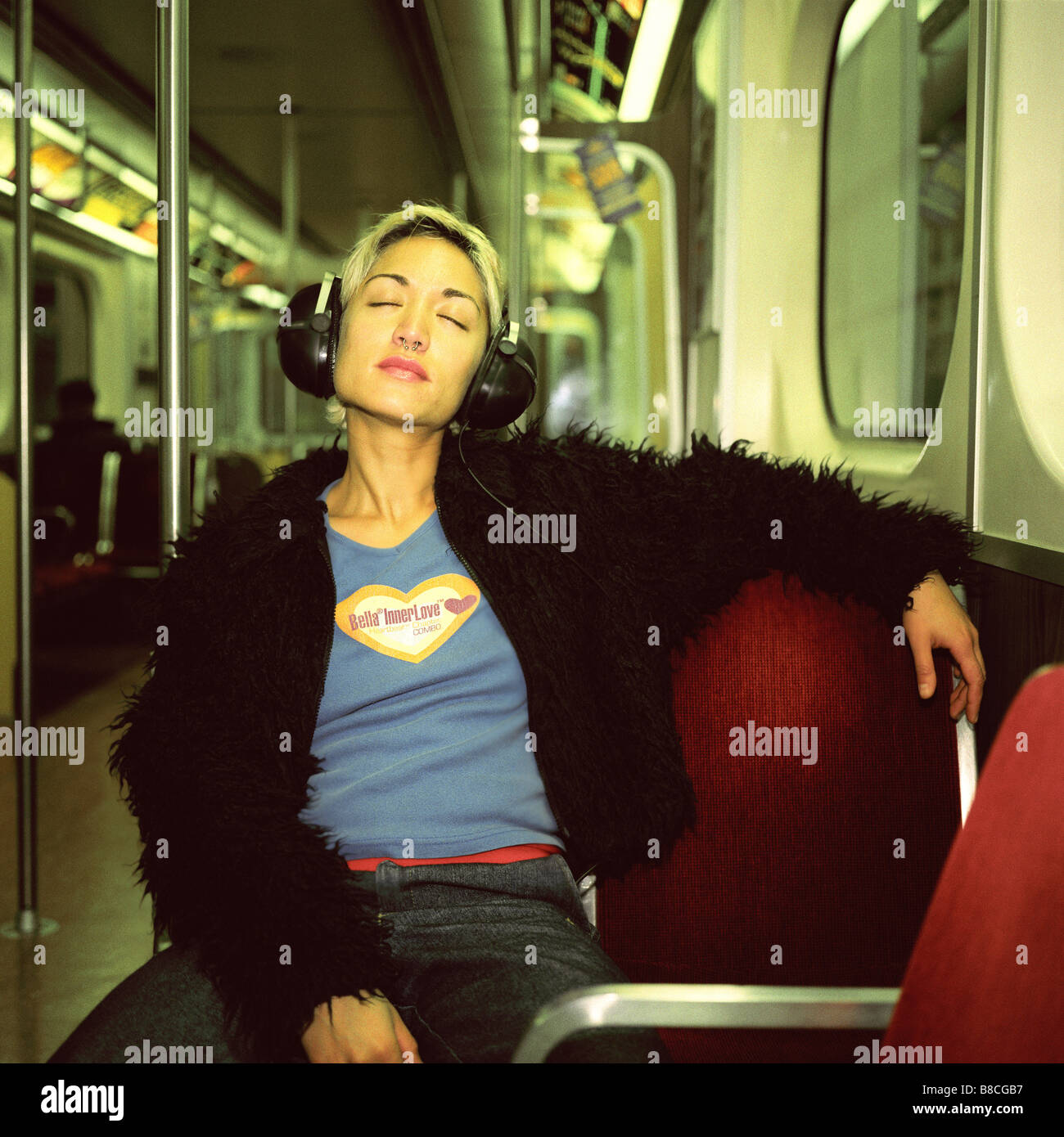 FL6303, Huy Lam; giovane donna che indossa le cuffie alla metropolitana sorridente cercando gli occhi chiusi Foto Stock