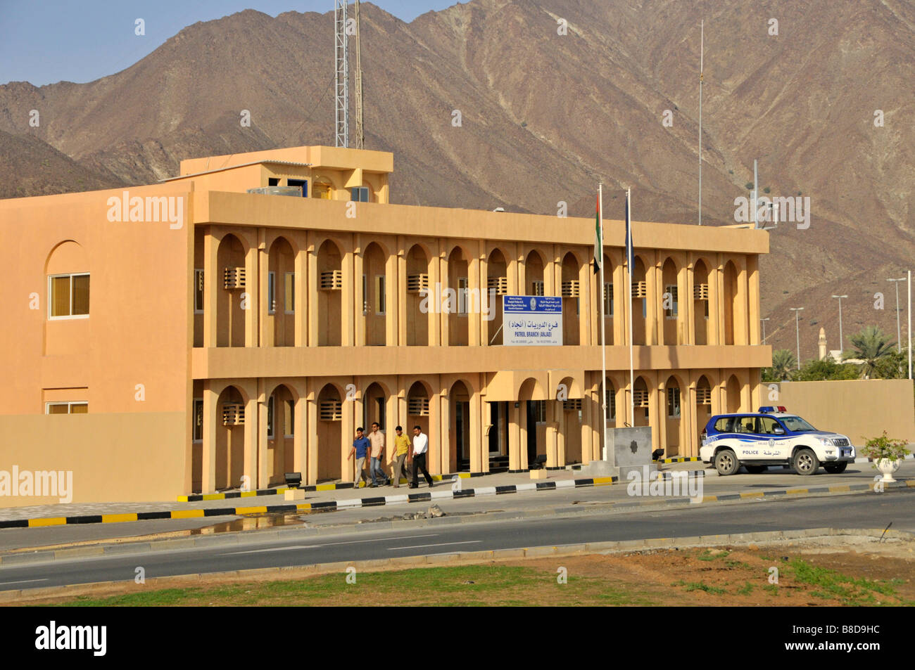 Facciata della stazione di polizia edificio moderno e auto della polizia all'esterno dell'emirato della regione orientale di Sharjah, arido golfo dell'Oman sullo sfondo collinare Foto Stock