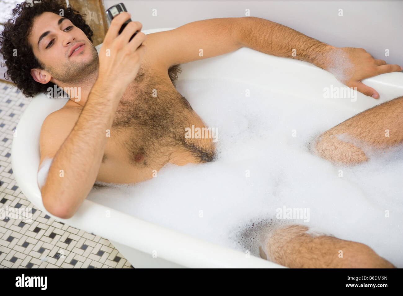 Uomo che utilizza un telefono cellulare nel bagno Foto Stock