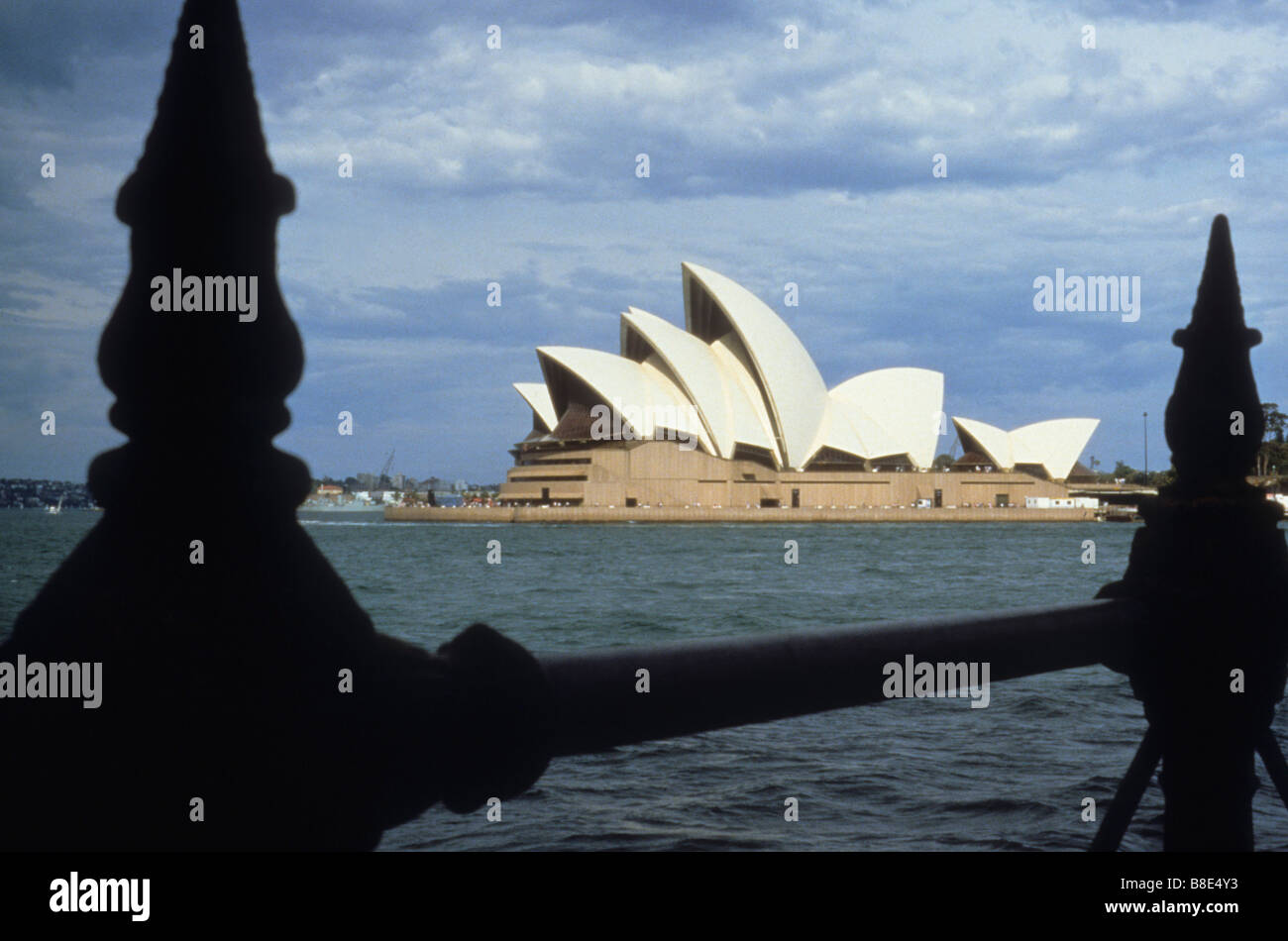 La Opera House di Sydney, Australia visto attraverso ornato pali da recinzione sul marciapiede in acqua Foto Stock