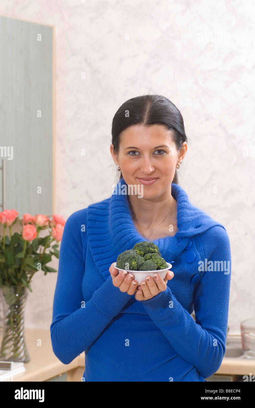 Donna in piedi in cucina tenendo una ciotola di broccoli verdi Foto Stock