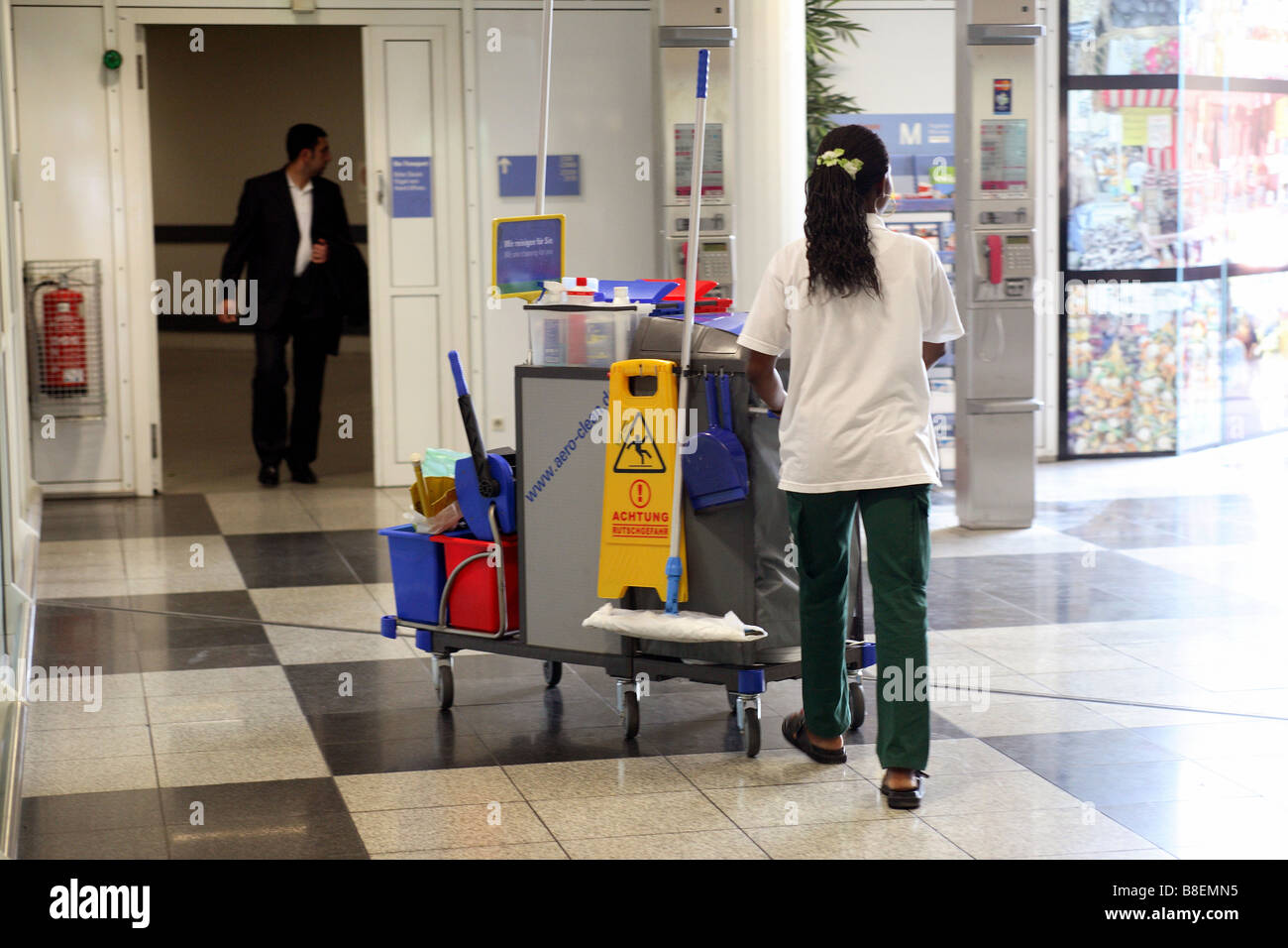 Donna delle pulizie a piedi attraverso la sala di attesa all'aeroporto di Monaco di Baviera, Germania Foto Stock