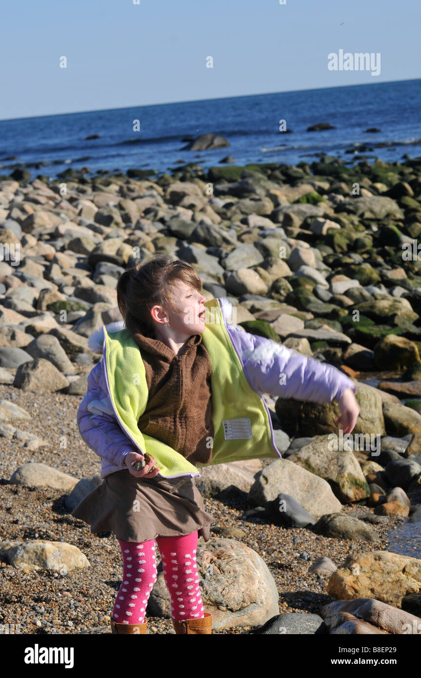 Giovane ragazza al bordo delle acque sulla costa rocciosa gettando rock in acqua Foto Stock