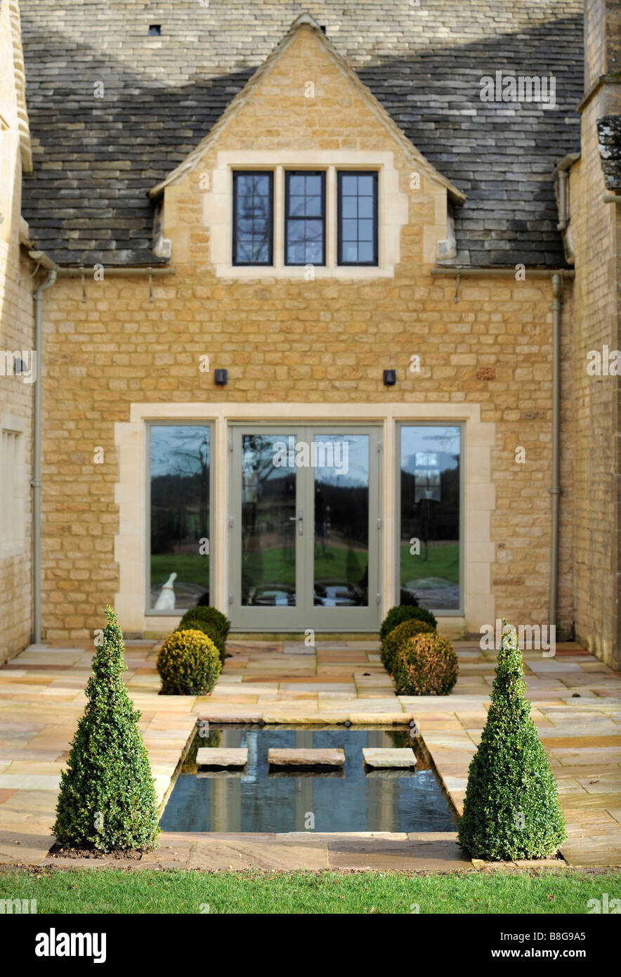 Un casale ristrutturato in Oxfordshire con un laghetto fiancheggiato da siepi di bosso, Regno Unito Foto Stock