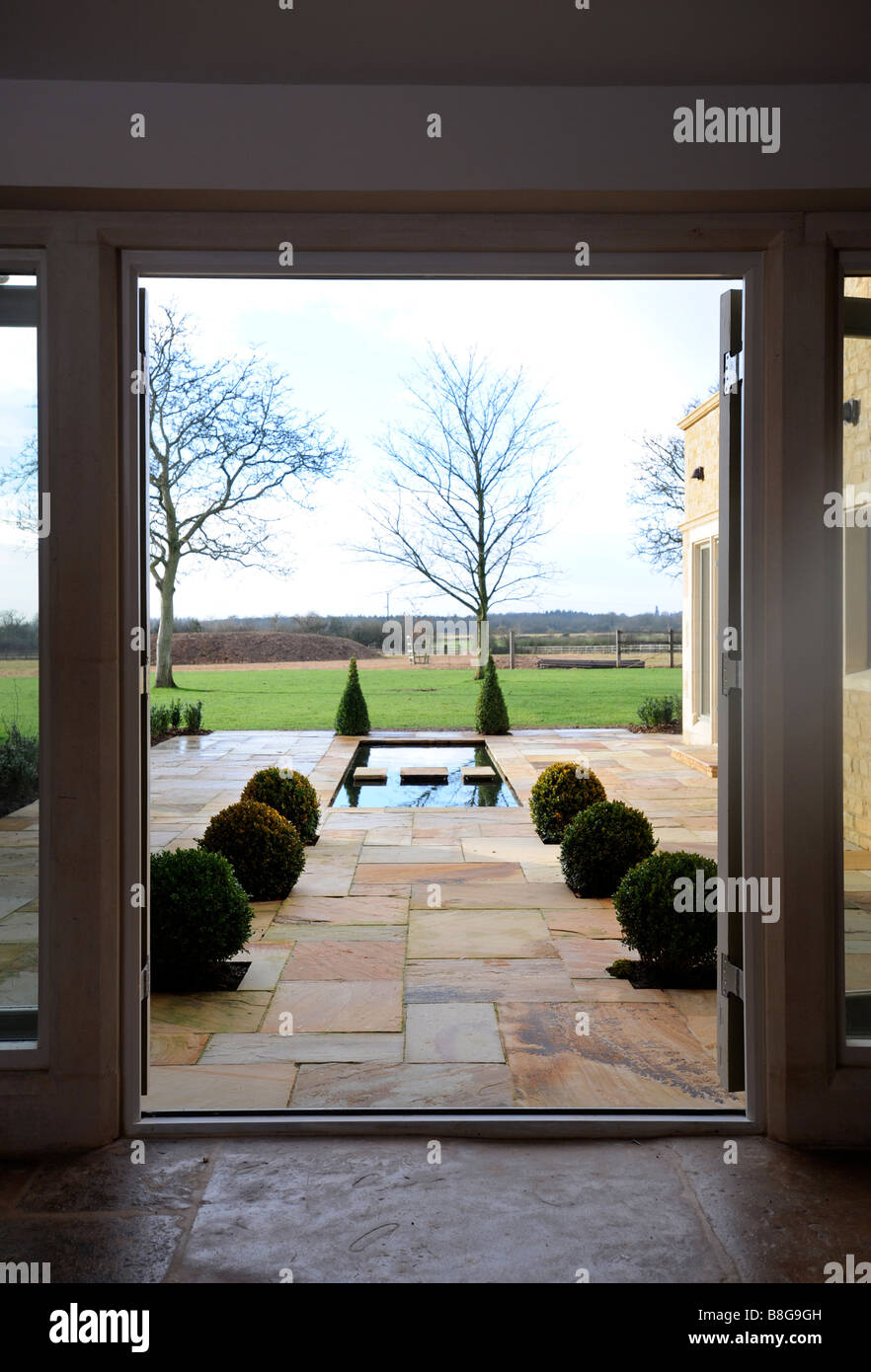 Un casale ristrutturato in Oxfordshire con un patio POND fiancheggiata da siepi di bosso, Regno Unito Foto Stock