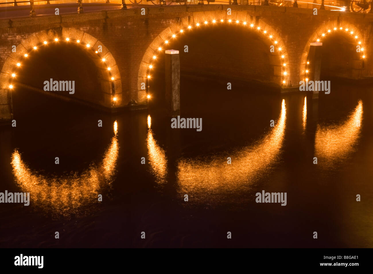 Ponte illuminato riflessa nel canale in una nebbiosa notte a Amsterdam Paesi Bassi Foto Stock
