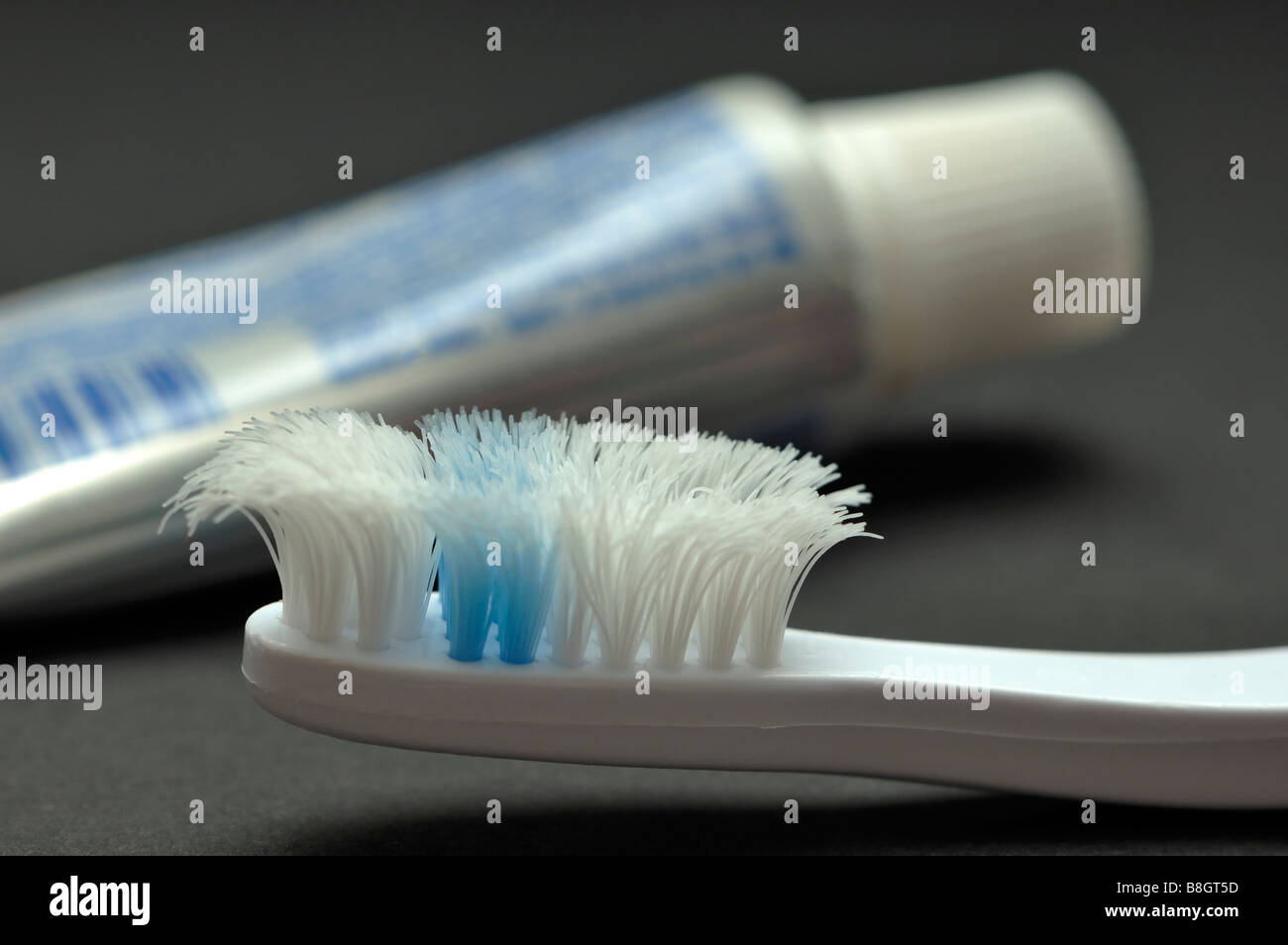 Primo piano di una molto usurati spazzolino da denti con un tubo di dentifricio in background Foto Stock