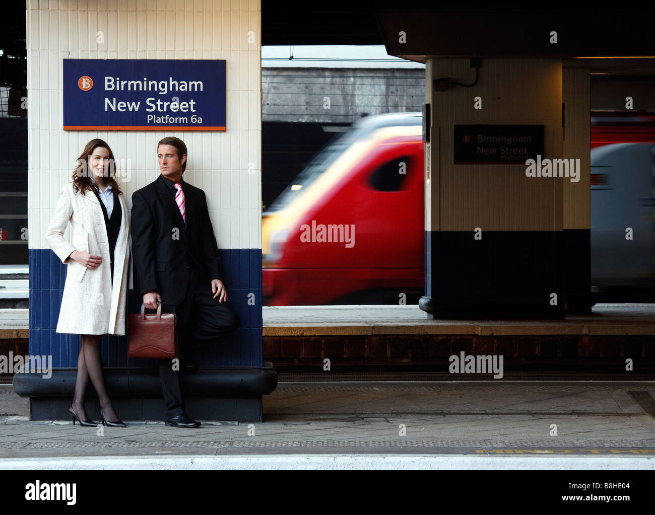 Imprenditore e la donna in una stazione ferroviaria piattaforma con un treno che va passato Foto Stock