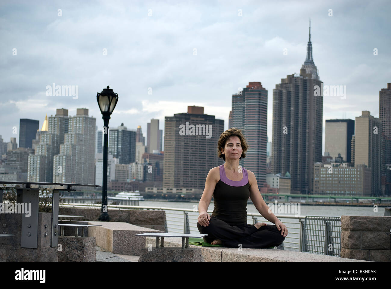 Donna fare yoga in gantry del Parco Statale di Long Island City, con skyline di Manhattan e l'Empire State Building dietro di lei Foto Stock