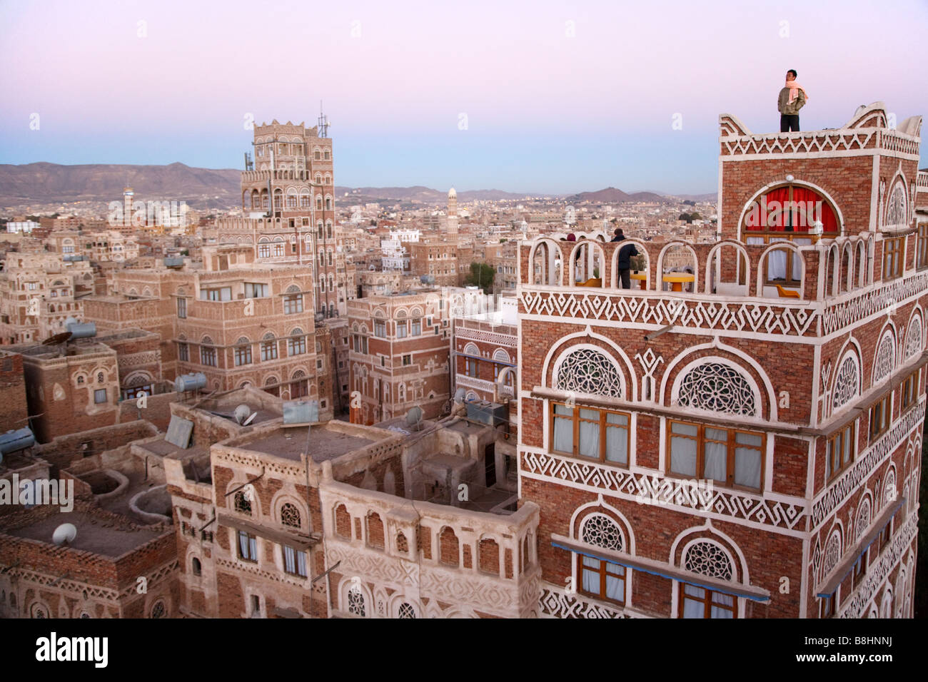 Un turista straniero sul tetto di un hotel tradizionale e paesaggio di Sana'a, la capitale dello Yemen presso il Morning twilight sunrise. Foto Stock