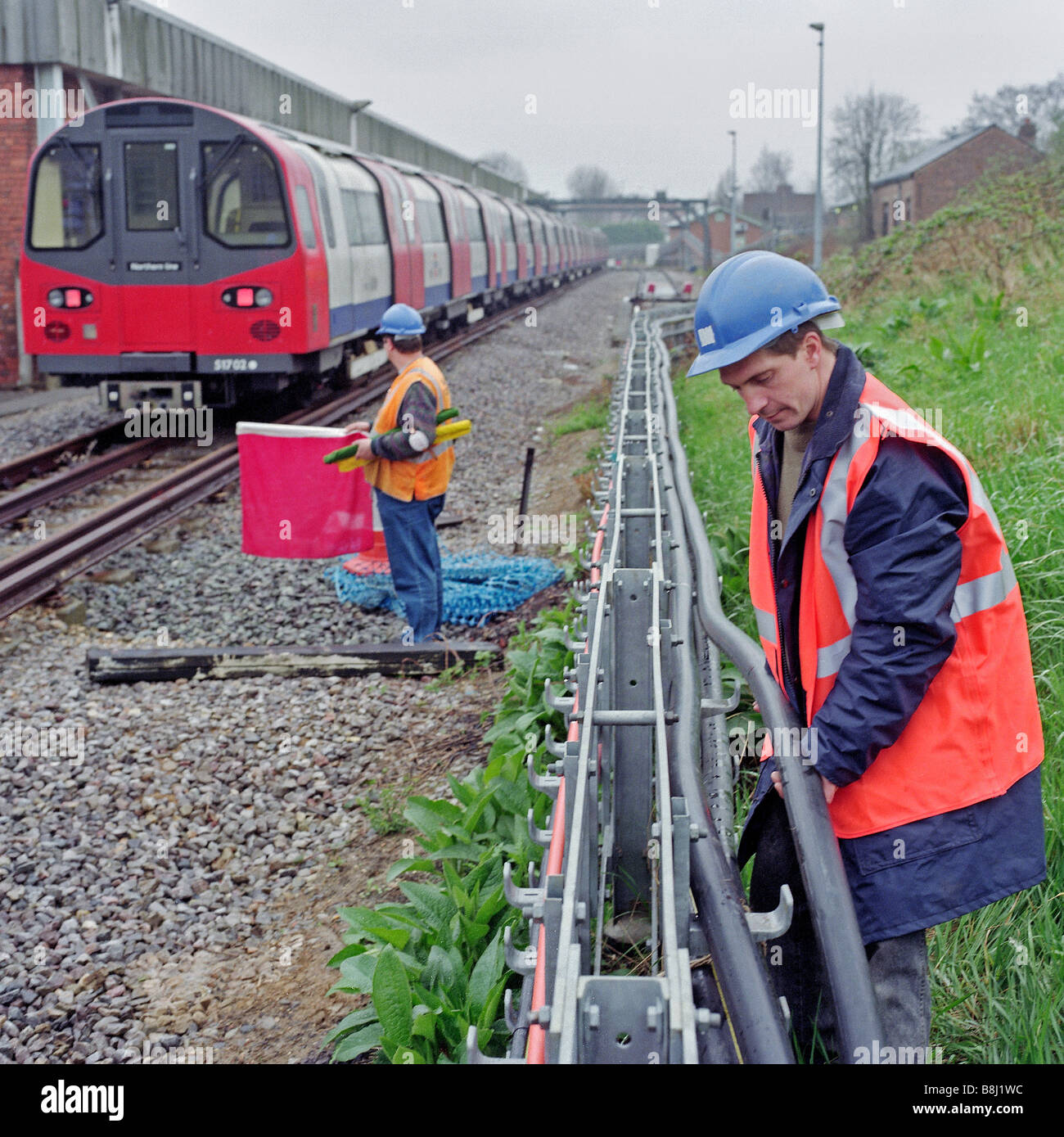Ingegnere di sostituzione cavo di alimentazione mentre un look-out detiene una bandiera rossa per garantire la sua sicurezza controllando i movimenti del treno. Foto Stock