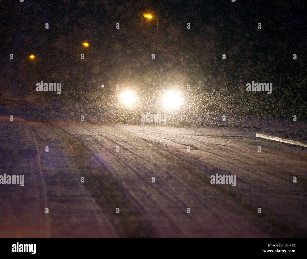 Una vettura i fari di notte come si aziona attraverso una tempesta di neve a Redditch, Worcestershire, Regno Unito Foto Stock