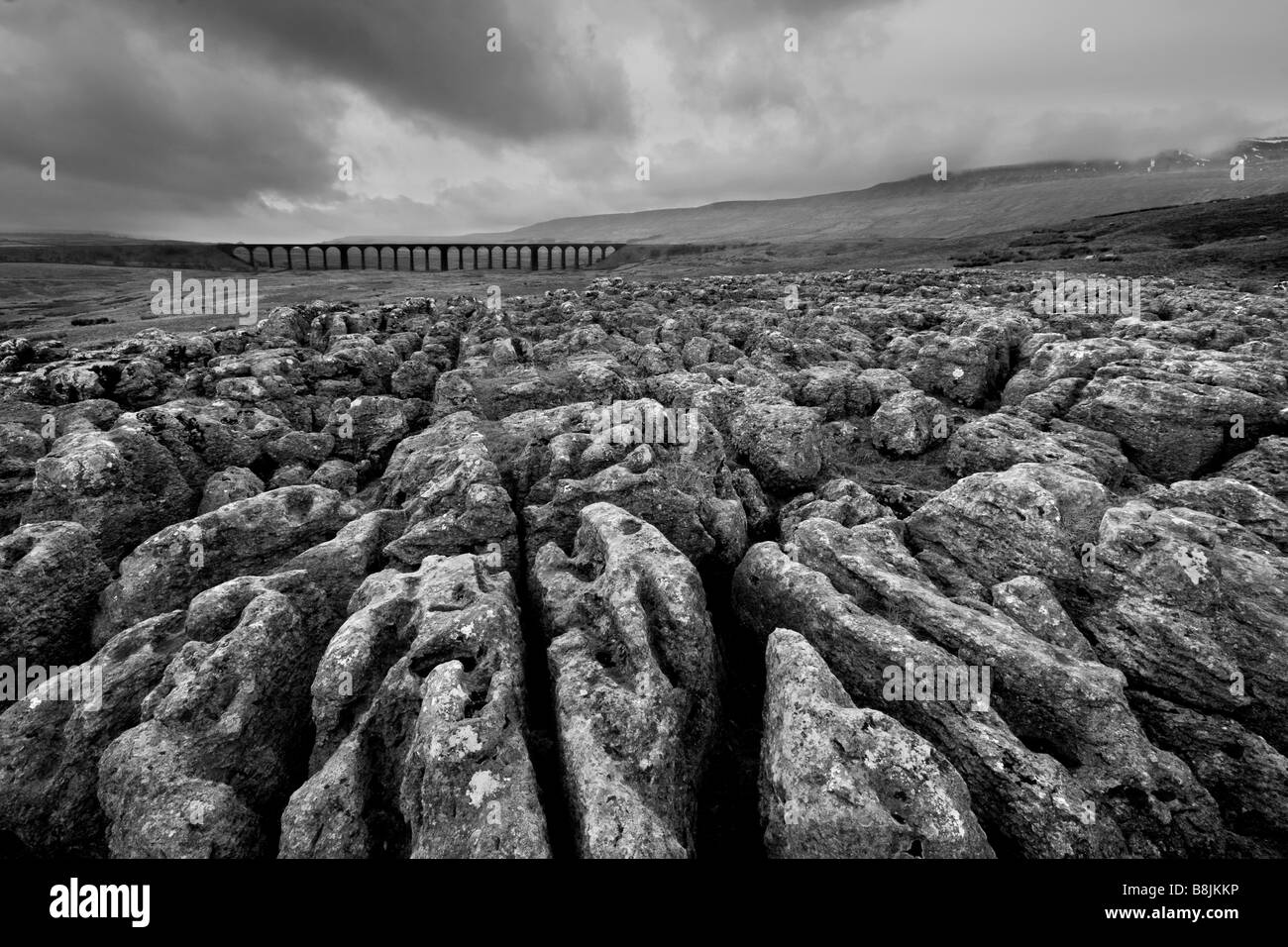 Nuvole temporalesche sulla pavimentazione di pietra calcarea con Ribblehead il viadotto in distanza, Ribblesdale, Yorkshire Dales, North Yorkshire Foto Stock
