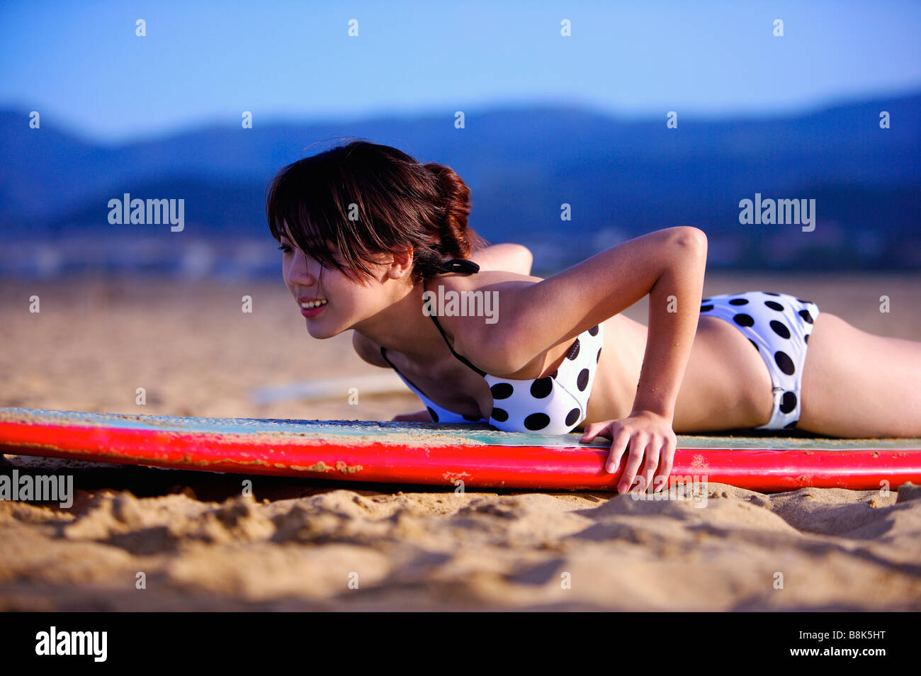 Giovane donna sdraiata sulla tavola da surf sulla parte anteriore e di pratica Foto Stock