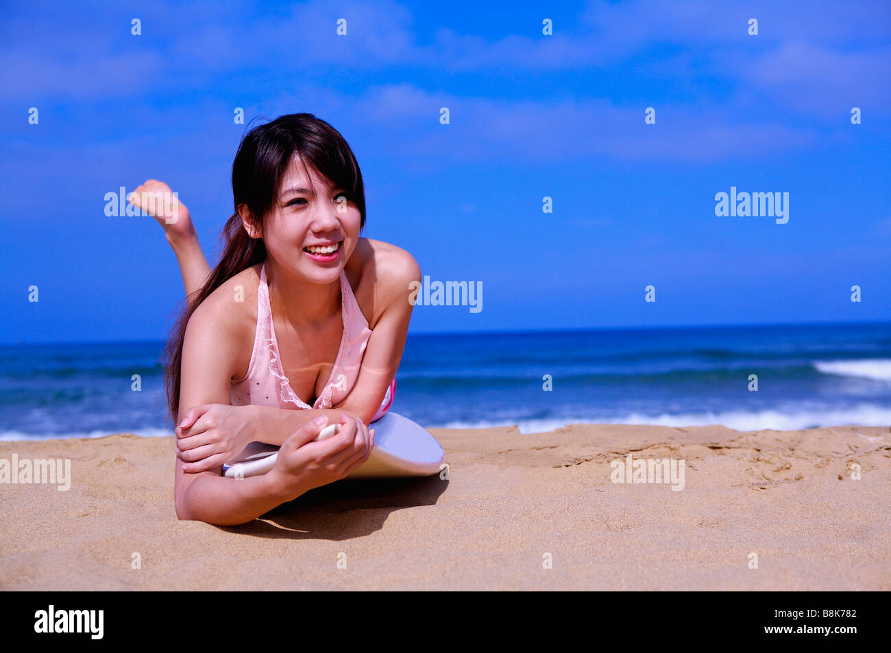 Giovane donna sdraiata sulla tavola da surf in spiaggia e guardando lontano sorridente Foto Stock