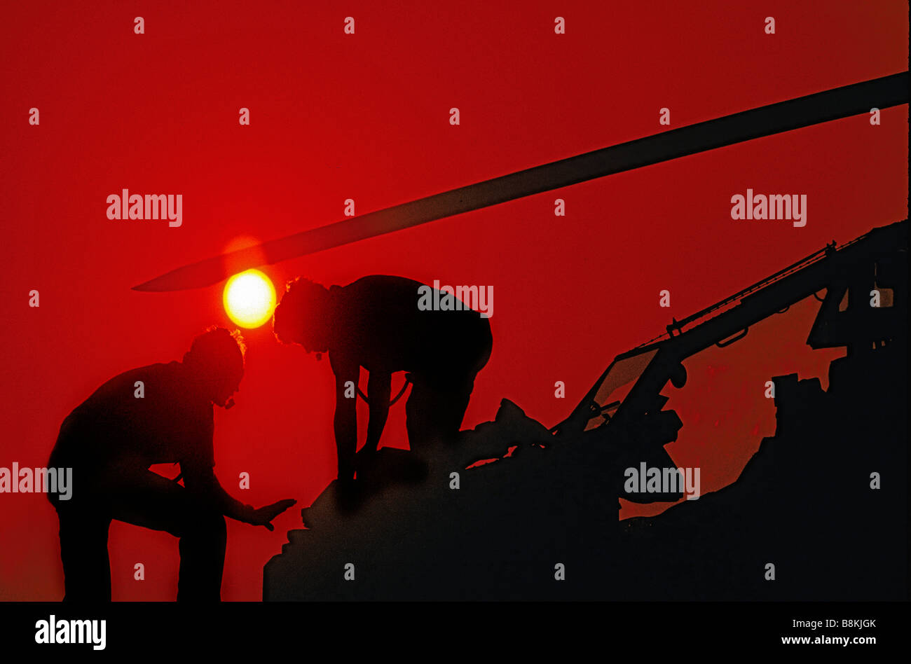 Silhouette con Sun di due tecnici aerospaziali lavorando sul naso dell'elicottero. Foto Stock