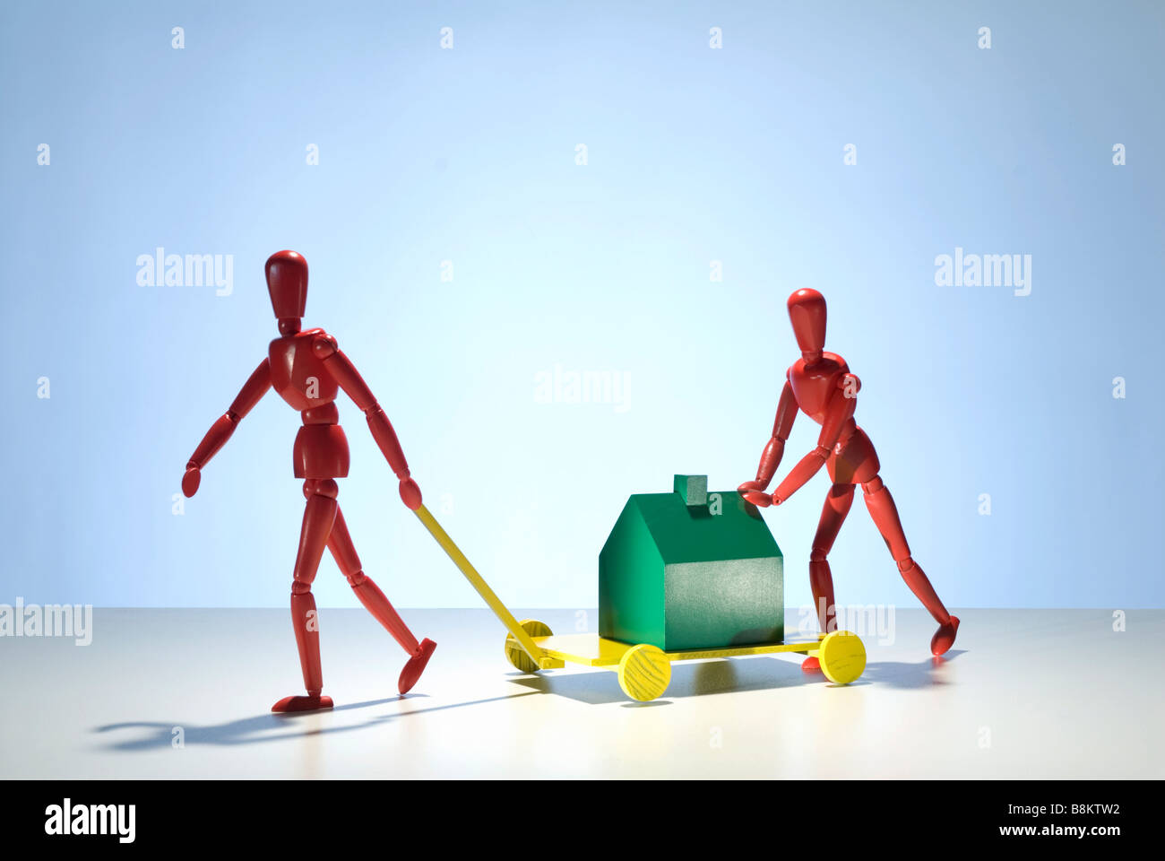 Due manichini di rosso le figure spostare un modello verde casa su un carro Foto Stock