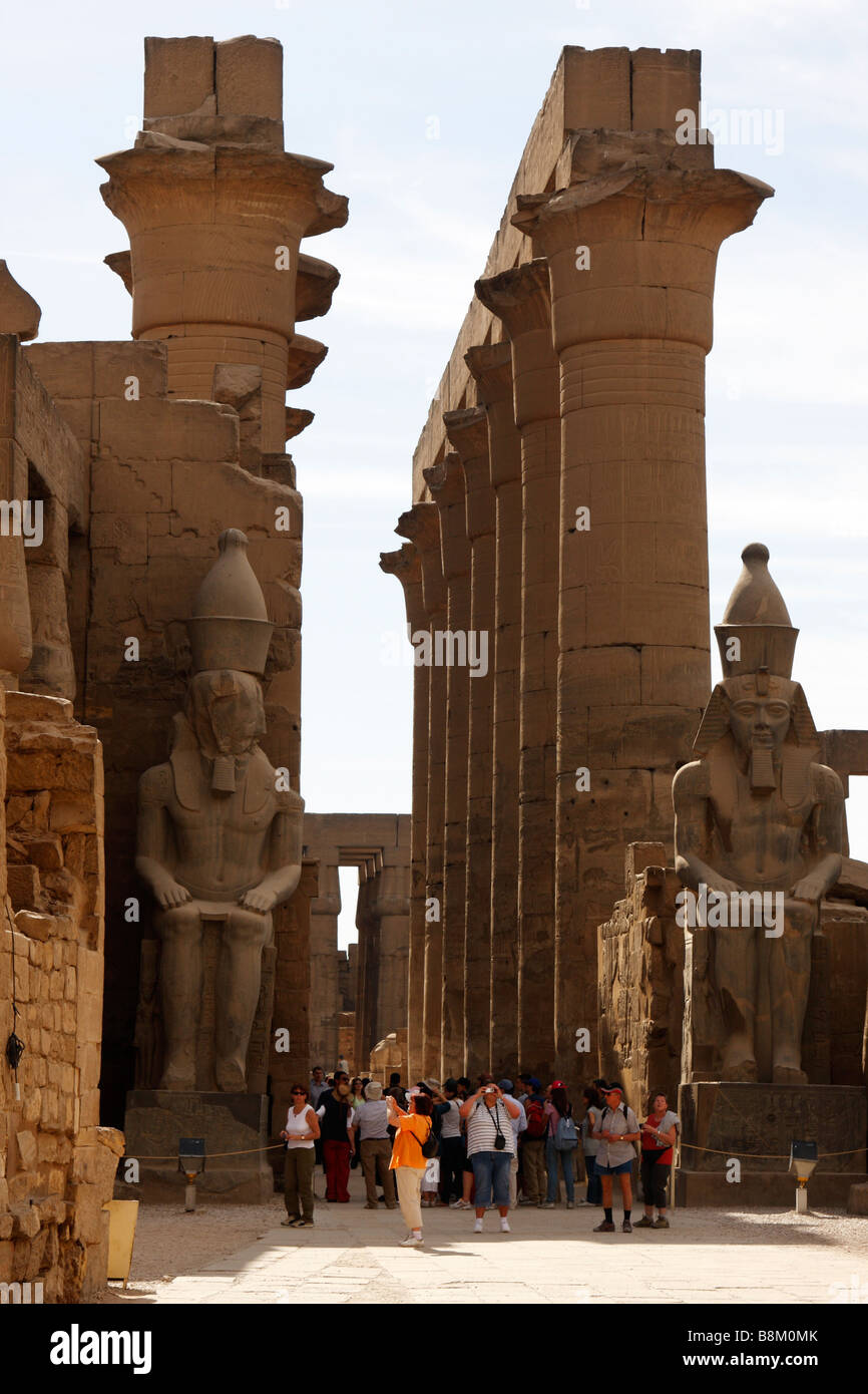 I turisti della Grande Corte di Ramses II stava sotto due colossali statue e Colonnato di Amenofi III, del Tempio di Luxor in Egitto Foto Stock