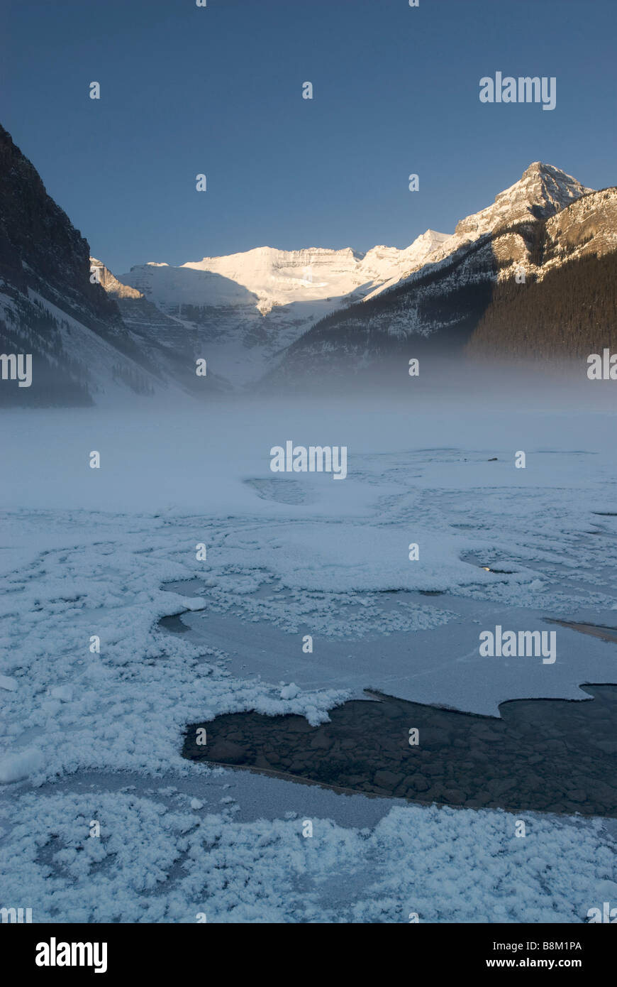 Sunrise colpisce le montagne dietro un lago ghiacciato Louise nel Parco Nazionale di Banff, Alberta, Canada. Foto Stock